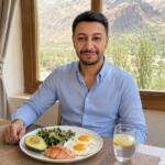 Shahbaz Ahmed founder of KetoFramework in a light blue shirt sitting at his Gilgit-Baltistan dining table with his first meal of the intermittent fasting eating window including eggs avocado leafy greens and salmon looking directly at camera with a warm satisfied smile representing how to break a fast and the best first meal after intermittent fasting